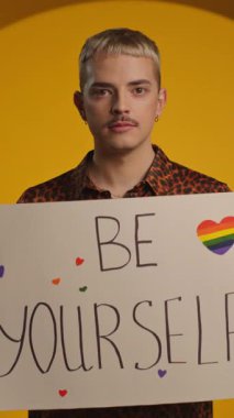 Pozitif genç gay adam elinde Igbt sloganıyla fotoğraf makinesine gülümsüyor.
