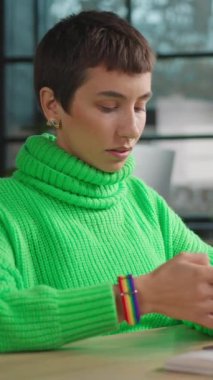 Açık yeşil kazaklı düşünceli transseksüel kadın akıllı telefonda sohbet ediyor.