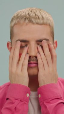 Makyajlı, elleri kameranın önünde olan genç ve ciddi eşcinsel bir adam.