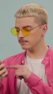 Pembe tişörtlü ve sarı gözlüklü genç adamın kapalı alanda akıllı telefon kullandığı bir stüdyo fotoğrafı.