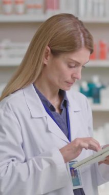 Kafkas sarışın olgun kadın eczanede ilaç reçetesi aramak için tablet bilgisayar aygıtı internet veritabanı kullanıyor..