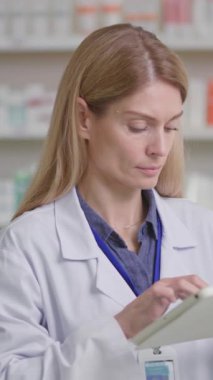 Profesyonel eczane çalışanı. Kafkasyalı sarışın kadının portresi. İşçi önlüğü giyiyor, tablet okuyor ve eczanede tıbbi bilgiler okuyor..