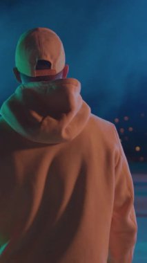 Hiphop tarzı erkek dansçısının arkasında sarı kıyafetli adam gece sahnesinin çatısında yürüyor ve şehir manzarasını seyrediyor. Sanatsal bir performans. Gece hayatı..