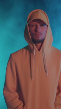 Dışarıda kameraya poz veren kapüşonlu sarı kıyafetli çekici hiphop bboy dansçısının portresi. Neon ve duman arka planı. Sahne. Performans. Eğlence.