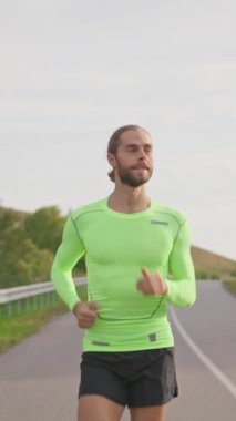 Kendine güvenen erkek koşucu bulutlu bir sabahta boş yolda koşuyor. Atletik genç sakallı sporcu dışarıda koşuyor. Şehir otoyolu. İnsanlar, eğlence ve spor.