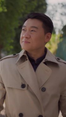 Gülümseyen yakışıklı Asyalı iş adamı şık bir sonbahar ceketi giyiyor sokakta yürüyor ve manzaraya hayran. Şehir insanları. Seyahat et. İşadamı.