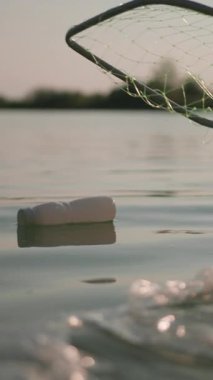 Tanınmayan kişi kirli nehirden çöp topluyor. Balık ağı. Su kirliliği. Su temizleme. Geri dönüşüm. Ekoloji.