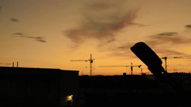 Huzurlu, huzurlu bir günbatımı sahnesi güzel siluetli vinçler, binalar ve canlı renkli bir gökyüzü sergiliyor.
