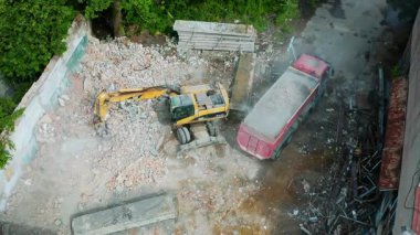 Toz ve molozlarla çevrili ağır makinelerle yıkılan yapılarla dolu yoğun bir inşaat alanı.