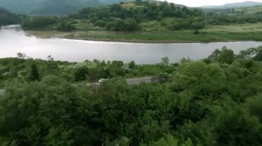 Huzurlu bir nehir ve yemyeşil dağlar boyunca uzanan güzel, dolambaçlı bir yolun büyüleyici manzarası.