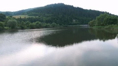 Yumuşak, cezbedici çevre aydınlatması ile yemyeşil tepeler çerçeveli, yumuşak dalgalı sakin bir nehir sahnesi