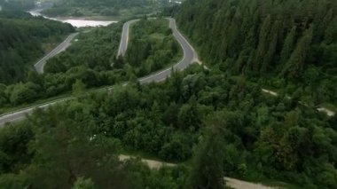 Nefes kesen manzaralı, gür, görkemli dağlar ve kıvrımlı bir yol, canlı yeşilliklerle kaplı.