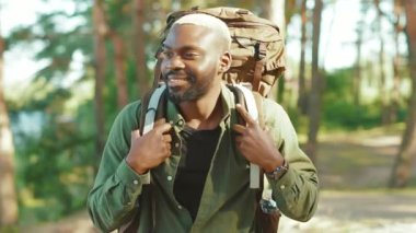 Afro-Amerikalı yürüyüşçü, turist sırt çantalı yakışıklı adam kameraya gülümseyerek tek başına seyahat ediyor. Pozitif siyah turist vahşi doğayı keşfediyor.