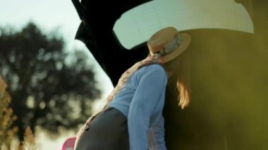 Şapka standı olan genç bir kadın bagajda bir şey arıyor. Gün batımının tadını çıkarıyor. Yüzeyde güneş ışığı tatili.