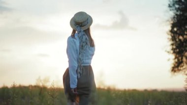 Güneş ışığında yürürken şapkalı mutlu bir genç kadın etrafına bakıyor sıcak doğa tatilleri yavaş çekimde genç portreler.