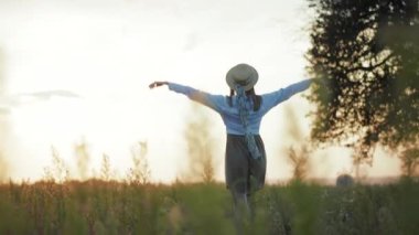 Yavaş çekim, güneş ışığında şapkalı kadın elini kaldırır. Sıcak doğa tatili tatili için ellerini kaldırır. Genç bir portre.