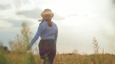 Gün ışığında, şapkalı bir kadın sıcak doğa tatillerinde yürür. Yavaş çekimde genç bir portre.