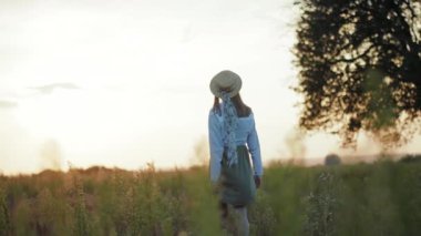 Güneş ışığında yürürken şapkalı kadın yakın plan çekimde elini kaldırıyor. Sıcak doğa tatili. Yavaş çekim portresi.