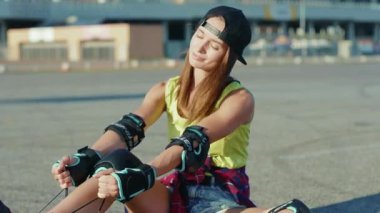 NEW YORK - 5 Nisan 2020: Güzel kız yerde oturuyor ve patenleri gülümsüyor. Mutlu ol. Yaz aylarında sokak bacakları ağır çekimde patenle kayıyor.