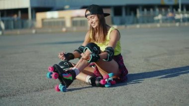 Genç bir kadın yerde oturuyor ve patenleri yerleştiriyor gülümsüyor. Yaz aylarında mutlu bir cadde. Ayaklar patenle kayıyor.