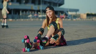 Portre genç kadın yerde oturuyor ve patenler koyuyor kameraya gülümseyen caddeye yaz aylarında bacaklar ağır çekimde patenle kayıyor