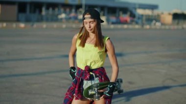 Ciddi çekici genç kadın kameraya bak. Ciddi biçimde kaykay tutuyor. Açık havada hippi tarzı sokak tarzı ağır çekim.