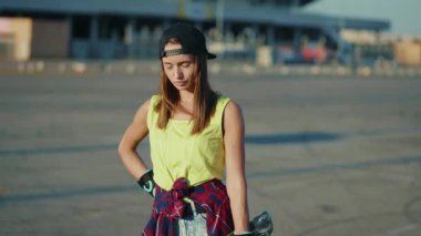 Yakın çekim çekici genç bayan ciddi bir kaykay tutuyor açık hava modasına uygun hippi sokak tarzı ağır çekim portresi