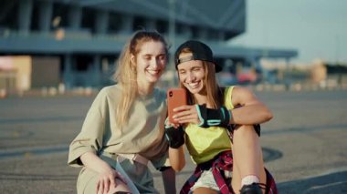 Patenlerle yerde oturan mutlu genç kadınlar yaz aylarında telefonla konuşur güler yüzlü caddelerde bacaklar ağır çekimde patenle kayar.