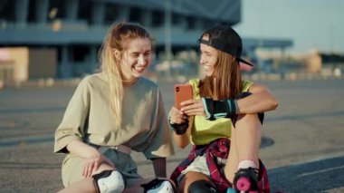 Kapalı yerde patenlerle oturan genç kadınlar telefonla konuşur güler yüzle güler yüzlü bir sokak hisseder yaz aylarında bacaklar ağır çekimde patenle kayar.