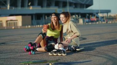 Yüzünde patenlerle oturmuş gülümseyen genç kadınlar telefonla konuşuyor. Yaz aylarında mutlu bir cadde. Bacakları kayıyor, ağır çekimde hareket ediyor.