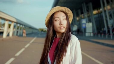 Pembe çantalı, gülümseyen kadın. Yavaş çekim çekici stil yolcusu kadın. Gün batımında havaalanında yürüyen güzel bir kadın. Ağır çekimde çekici, ince 25 'li yaşlarda esmer, uzun saçlı, bavulları üzerinde yürüyen Asyalı kadınlar.