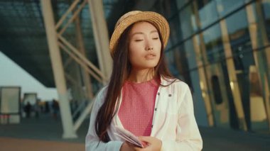 Havalimanı dışında uçuş biletlerini bekleyen sıradan giysili çekici, genç Çinli bir kızın portresi kameraya harika görünüyor. Asyalı kadın gezgin.
