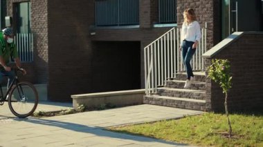 Kasklı ve tıbbi maskeli bir erkek kurye, müşteriye bisiklet çekici kadın eşliğinde kese kağıdıyla yemek getiriyor. Dışarıda durup Coronavirus siparişi veriyor.