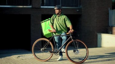 Kapalı portre çekici teslimatçı bisikletli sırt çantası ile şehir iş kamerasına bakıyor kurye kargo paketi ağır çekim