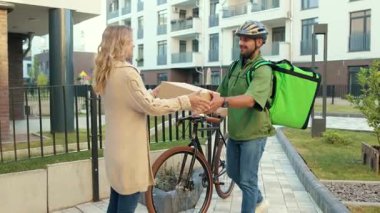 Genç adam kuryesini güvenlik kaskıyla kapat. Müşteriye bisikletli çekici bir kadınla kutuyu teslim et. Dışarıda dur ve ağır çekim sipariş et.