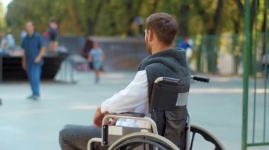 Tekerlekli sandalyede oturan depresif adamı vurdu parkta oyun parkına baktı üzgün hissetti. Felç olmuş hastalıklar sağlık hizmetleri umutsuzluk bozukluğu. Yavaş çekim