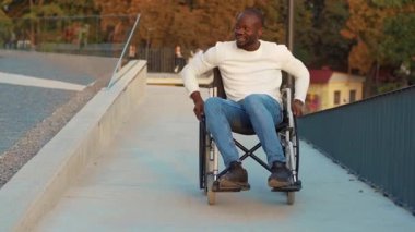 Mutlu yakışıklı engelli adam gün ışığında tekerlekli sandalyeye biniyor, gülümsüyor ve parkta şarkı söylüyor. Felç yetersizliği pozitif engelli. Yavaş çekim