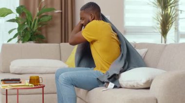 Sağlıksız Afro-Amerikalı genç adam evde kalıp ateş enfeksiyonu kapmak için battaniyeye sarılmış. Coronavirus belirtileri. Salgın. Karantina konsepti.