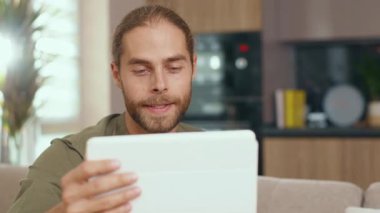 Tablet bilgisayar kullanan yakışıklı beyaz bir adam ekranda kayan web sayfalarında geziniyor oturma odasında mesajlaşan mesajlarla görüntülü sohbet ediyor. Erkek yüzü p-portresi. Aygıtlar.