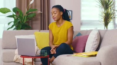 Çekici, mutlu, genç, Afrikalı bir kadın uzak bir arkadaşla görüntülü sohbet ediyor gülümsüyor, eğlenceli ev eğlencesi aletleri kullanıyor, teknolojiyi içeride kullanıyor..