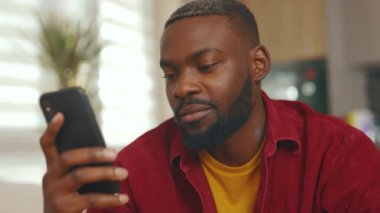 Ciddi bir Afro-Amerikan erkeğiyle yüzleş. Evdeki kanepede otur. Sosyal medyada iletişim kurmak iş uygulamasını gevşetiyor. Yakışıklı, ciddi bir adam. - İnternet. Yavaş çekim
