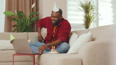 Karantina sırasında online doğum günü kutlaması için dizüstü bilgisayar kullanan Afro-Amerikalı genç adam. İletişim ağı sosyal mesafesi. Yavaş çekim