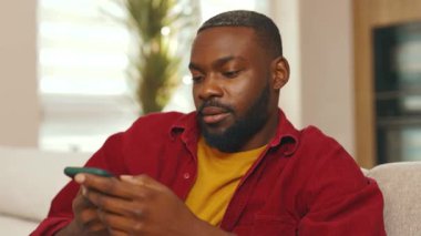 Portre Afro-Amerikan genç adam sesli mesaj kaydediyor sosyal ağdaki telefonu kullanıyor. Kapalı alandaki kablosuz iletişim teknolojisi mikrofon hoparlörünü kullanarak gülümsemek. Yavaş çekim