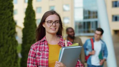 Üniversite kampüsünün yakınında kameraya gülümseyen, çizgili tişörtlü çekici Avrupalı kızın açık hava portresi. Kadın güzelliği. Akıllı kadın konsepti.