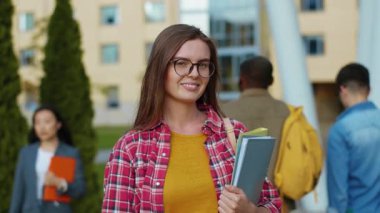 Kitapları üniversitede duran çekici esmer bir kadın. Kameraya gülümseyen şık üniversiteli bir kızın portre yüzü. Akıllı nesil. Dişiler.