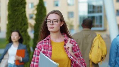 Güzel beyaz kız öğrenci çantasını ve kitaplarını tutarak kampüs üniversitesinin yanında, modern binanın dışında ders bekliyor. Üniversiteli kız konsepti.