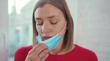 Endişeli genç kadın pencere pervazına oturmuş tıbbi yüz maskesi takıyor koronavirüs kendini tecrit depresyon penceresi sıkıcı ağır çekim