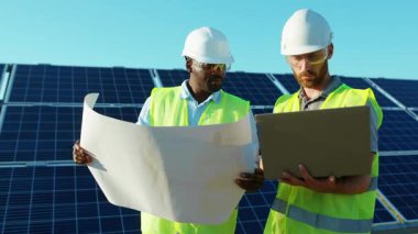 Ciddi adamlar güneş çiftliğinde dizüstü bilgisayar ve proje planı kullanıyorlar. Güneşli bataryaların montajını tartışıyorlar. Afrika kökenli Amerikan elektriği yavaş çekim.