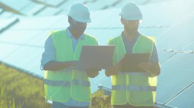 Mühendisler güneş çiftliğinde dizüstü bilgisayar kullanıyorlar. Yürürken güneşli bataryaların kurulumunu tartışıyorlar. Afrika kökenli Amerikan elektriği yavaş çekim.