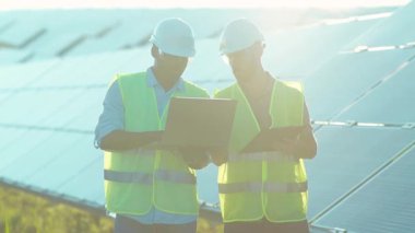 Güneş çiftliğinde insanlar özel üniformalı dizüstü bilgisayar kullanıyorlar. Güneşli pillerin kurulumu hakkında konuşuyorlar. Afrika kökenli Amerikan elektriği yavaş çekim.